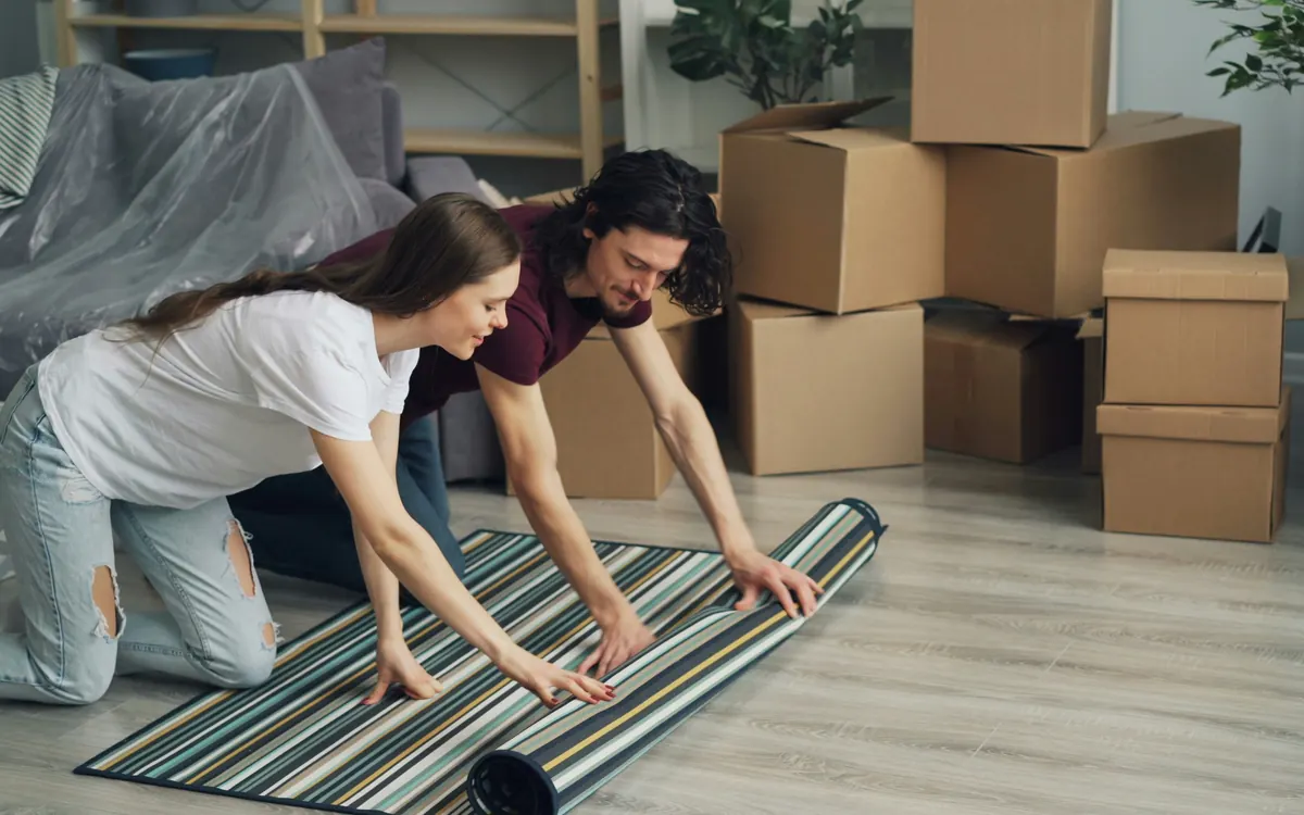 Couple unrolling a rug together among moving boxes