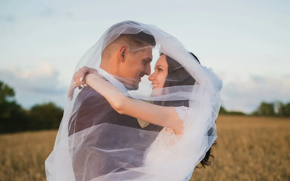 Newlyweds embracing outdoors beneath a wedding veil