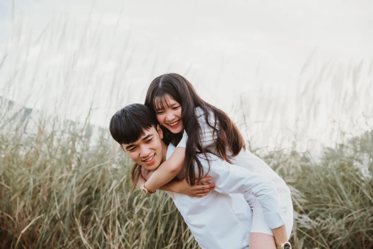 A smiling couple enjoying a piggyback ride in tall grass